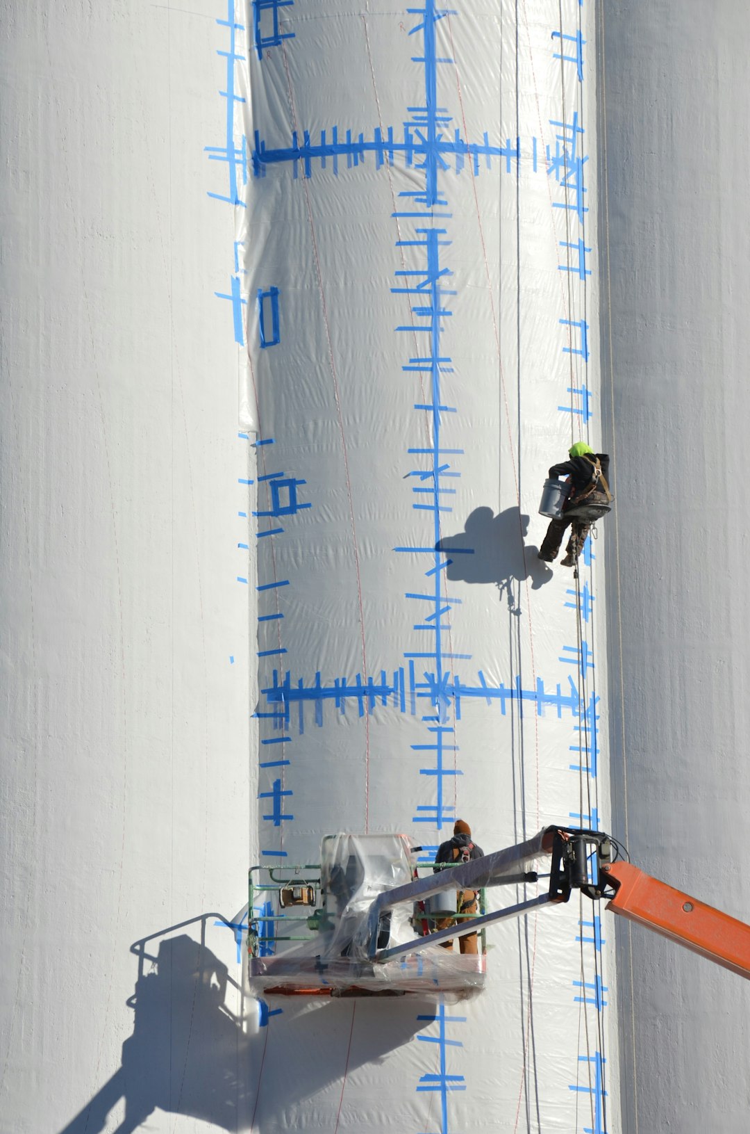 Repainted silos being prepped for a USA Flag Mural by workers in man lift and suspended by cables